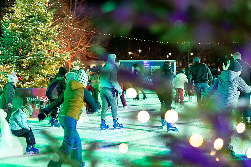 Im Bild sind Menschen zu sehen, die auf einer beleuchteten Eisbahn Schlittschuh laufen.