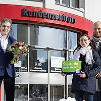 zwei männer und eine frau stehen vor einem gläsernen gebäube und präsentieren einen blumenstrauß