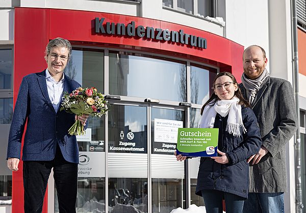 zwei männer und eine frau stehen vor einem gläsernen gebäube und präsentieren einen blumenstrauß