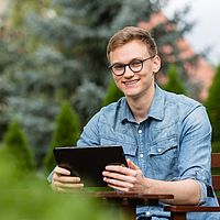 ein mann in einem blauen hemd hat ein tablet in der hand und lächelt in die kamera