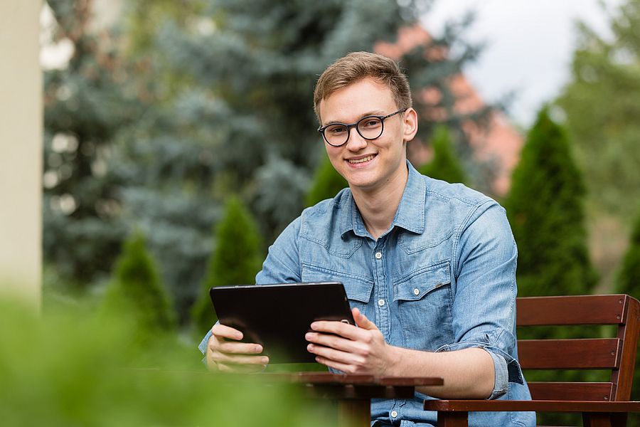 ein mann in einem blauen hemd hat ein tablet in der hand und lächelt in die kamera
