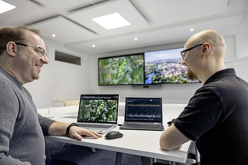 Zwei Männer, Martin Runge und Lucas Eib, sitzen an einem Tisch mit zwei Laptops und unterhalten sich.