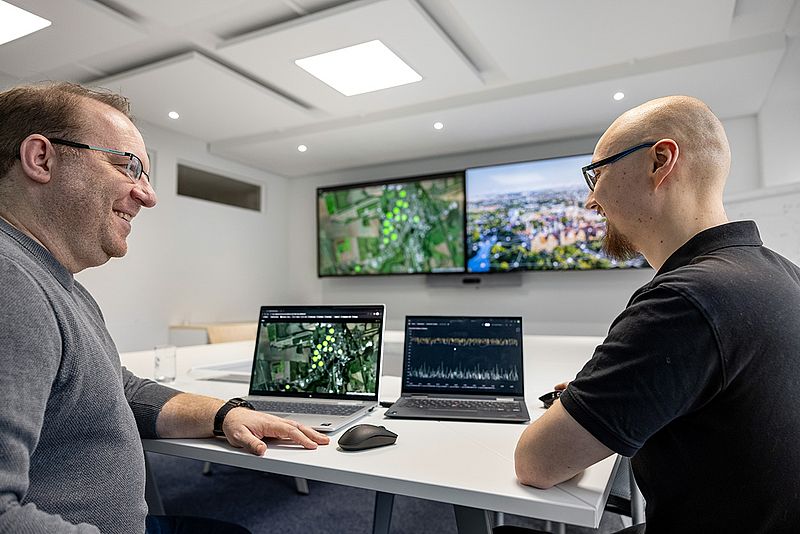 Zwei Männer, Martin Runge und Lucas Eib, sitzen an einem Tisch mit zwei Laptops und unterhalten sich.