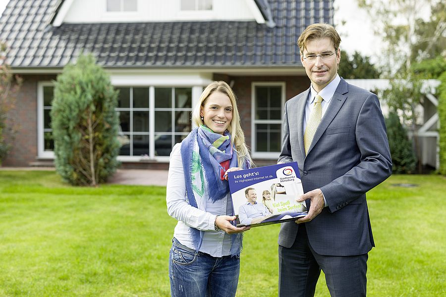 Vertriebsleiter Helge Gerullis begrüßt Carolin Steinert als 1000. Kundin am Breitbandnetz in Merseburg ein mann und eine frau stehen auf einer wiese vor einem haus