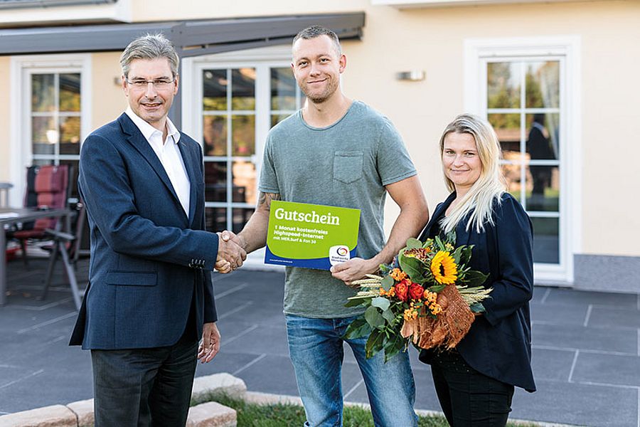 2 personen bekommen von einem mann im anzug einen preis überreicht