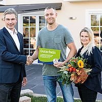 2 personen bekommen von einem mann im anzug einen preis überreicht