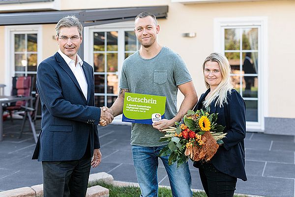 2 personen bekommen von einem mann im anzug einen preis überreicht