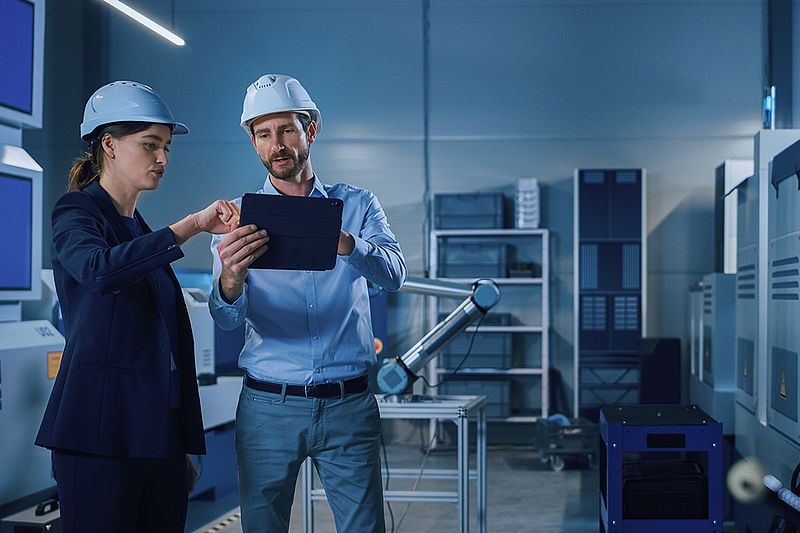 zwei arbeiter mit bauhelm stehen in einer produktionshalle und unterhalten sich