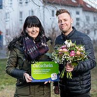 ein mann und eine frau stehen auf einer wiese vor einem haus mit einem blumenstrauß in der hand