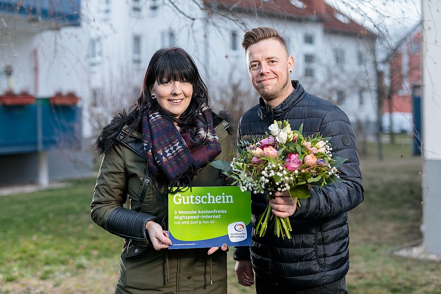 ein mann und eine frau stehen auf einer wiese vor einem haus mit einem blumenstrauß in der hand
