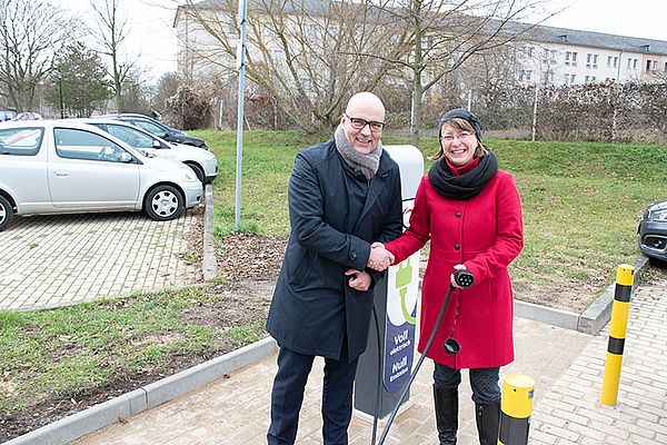ein mann und eine frau reichen sich an einem parkplatz die hände und schauen in die kamera
