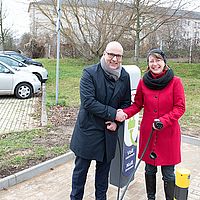 ein mann und eine frau reichen sich an einem parkplatz die hände und schauen in die kamera