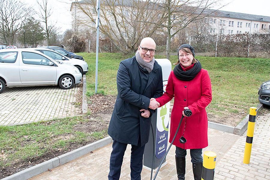 ein mann und eine frau reichen sich an einem parkplatz die hände und schauen in die kamera