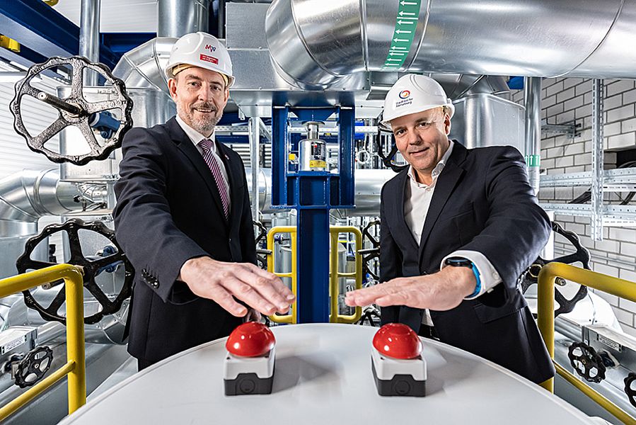 zwei personen im anzug stehen in einer produktionshalle und drücken inen roten busser