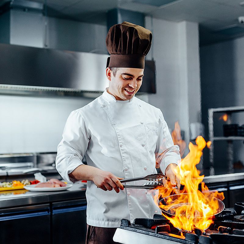 ein koch hält eine pfanne über ein offenes feuer