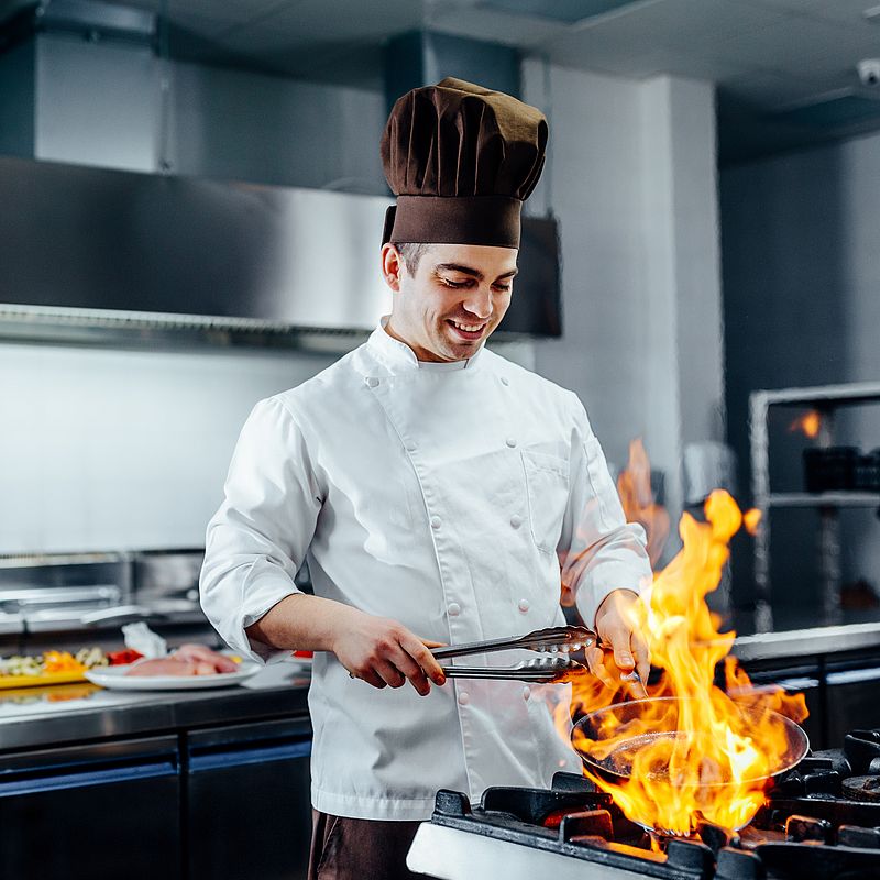 ein koch hält eine pfanne über ein offenes feuer