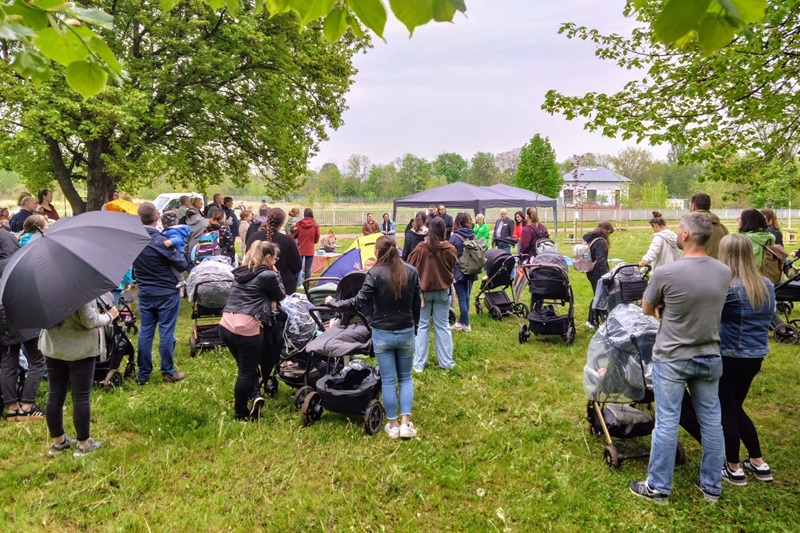 Auf einer Wiese stehen Menschen, vor allem Familien, vor einem Pavillon während einer Ansprache.