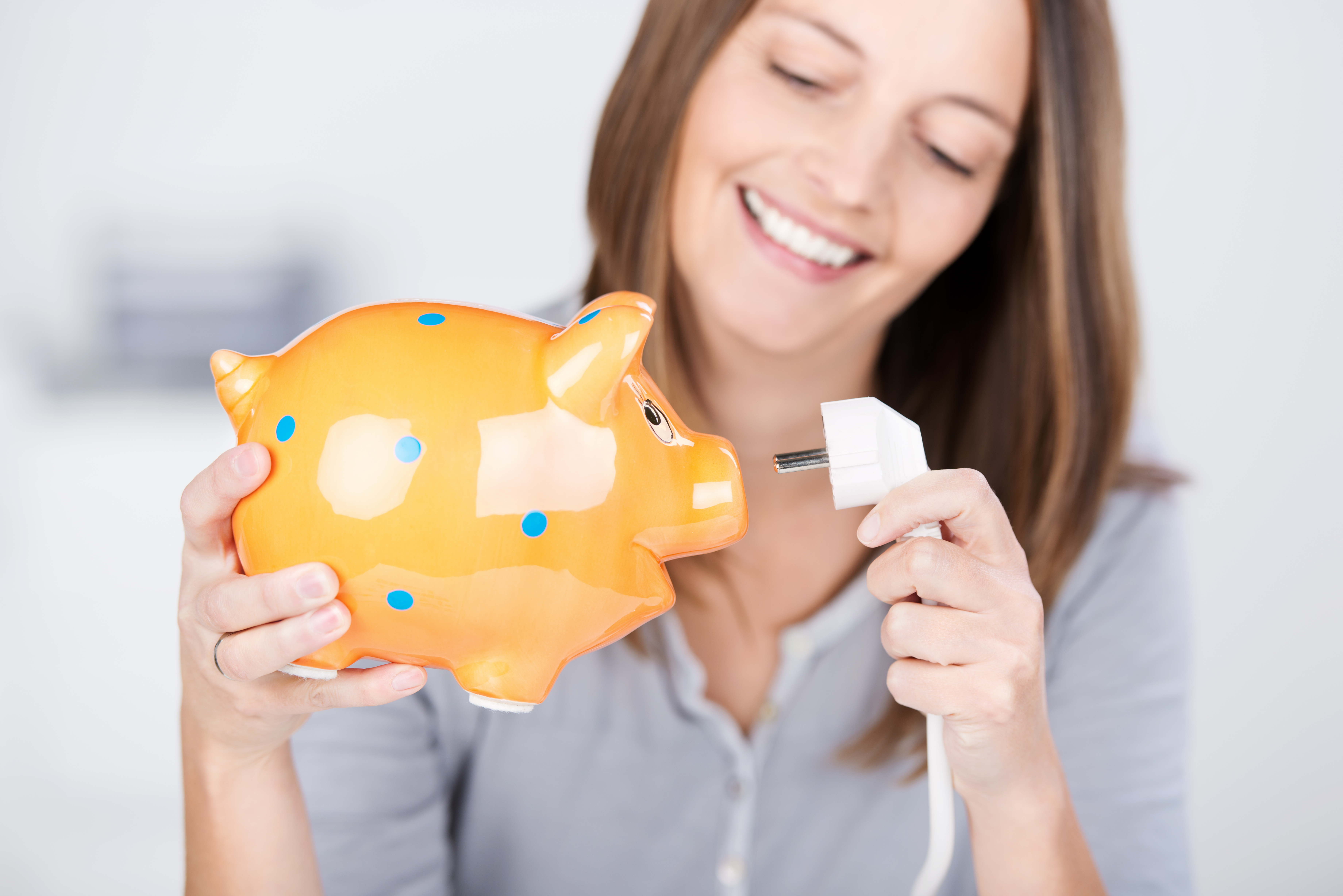 eine lächelnde frau hat ein sparschwein und ein kabel in der hand